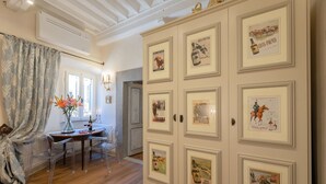 A room with a wooden floor, a table with chairs, a vase with flowers, and a door with framed pictures. - Cosy apartment for 2 people with WIFI, A/C and TV (Cortona)