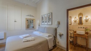 A bedroom with a large bed, a bedside table with a lamp, and a bathroom with a sink and mirror. - Cosy apartment for 2 people with WIFI, A/C and TV (Cortona)