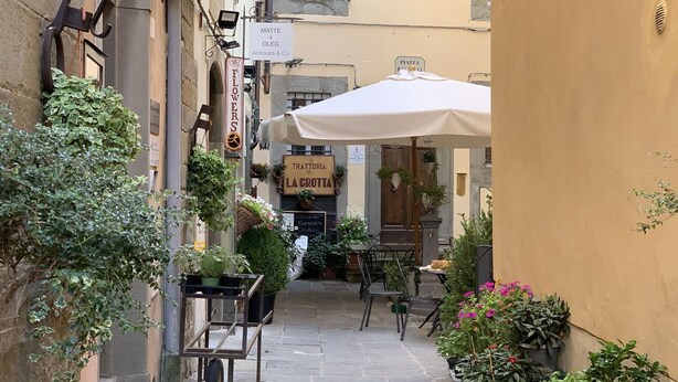 A narrow street with outdoor seating, potted plants, and a sign for 'Trattoria La Crotta'. - Cosy apartment for 2 people with WIFI, A/C and TV (Cortona)
