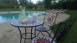 A poolside setting with a mosaic-tiled table and chairs, a glass pitcher, and a glass.