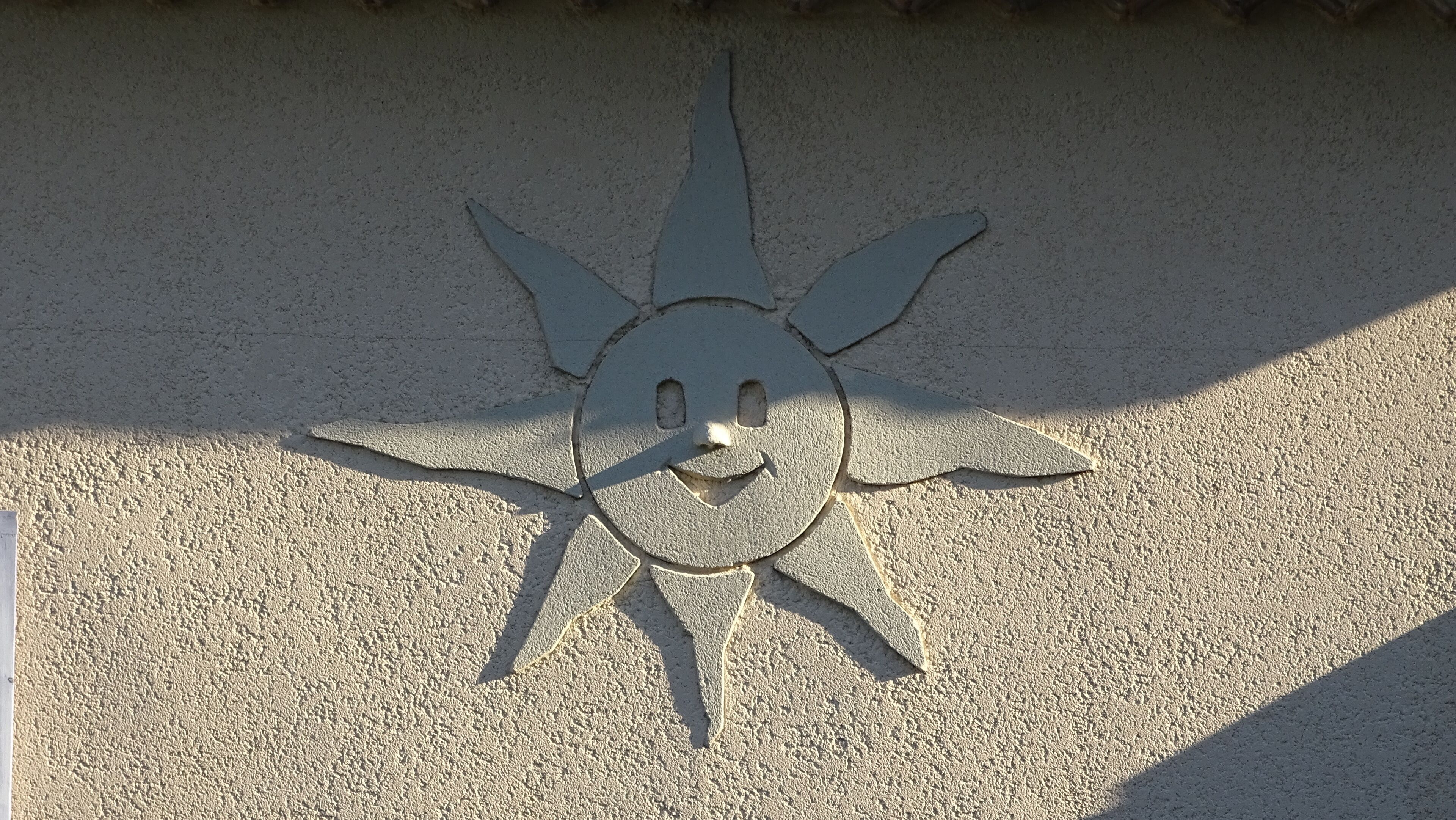 Una escultura con forma de sol y rostro sonriente sobre una superficie texturizada.