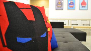 A room with a grey sofa and a Superman-themed pillow.