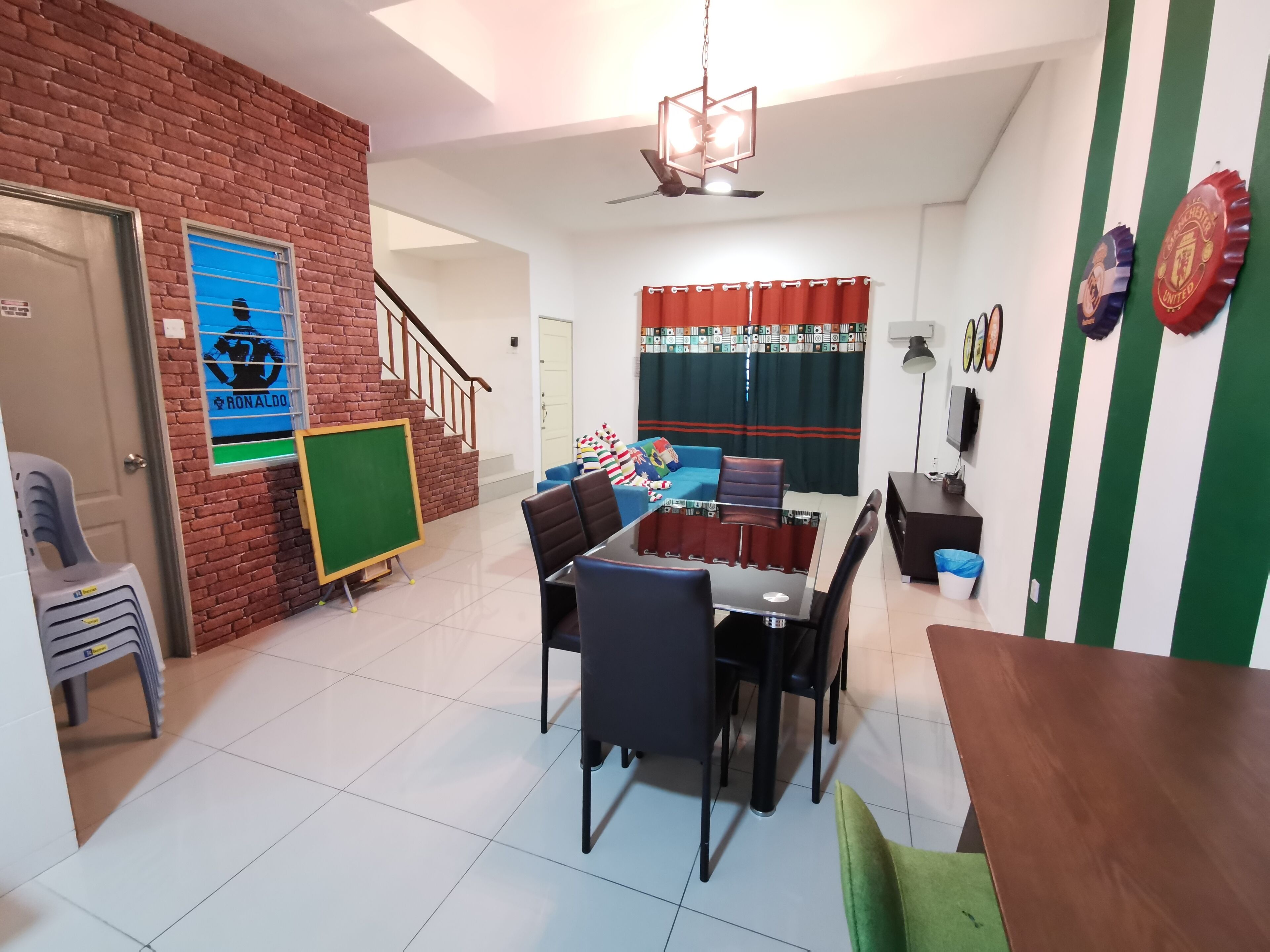 A living room with a brick wall, a green chalkboard, a dining table with chairs, a sofa, and a TV.