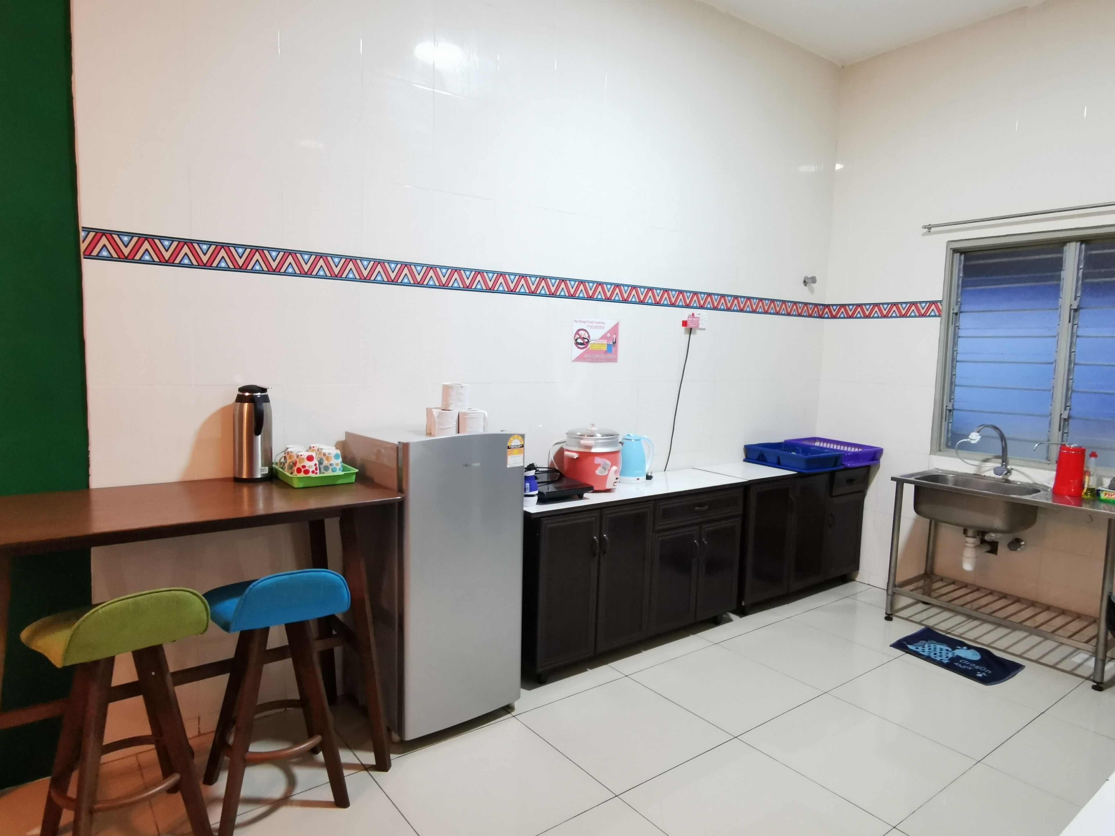 Una cocina compacta con refrigerador, pileta y ventana. Hay taburetes y una pequeña mesada.