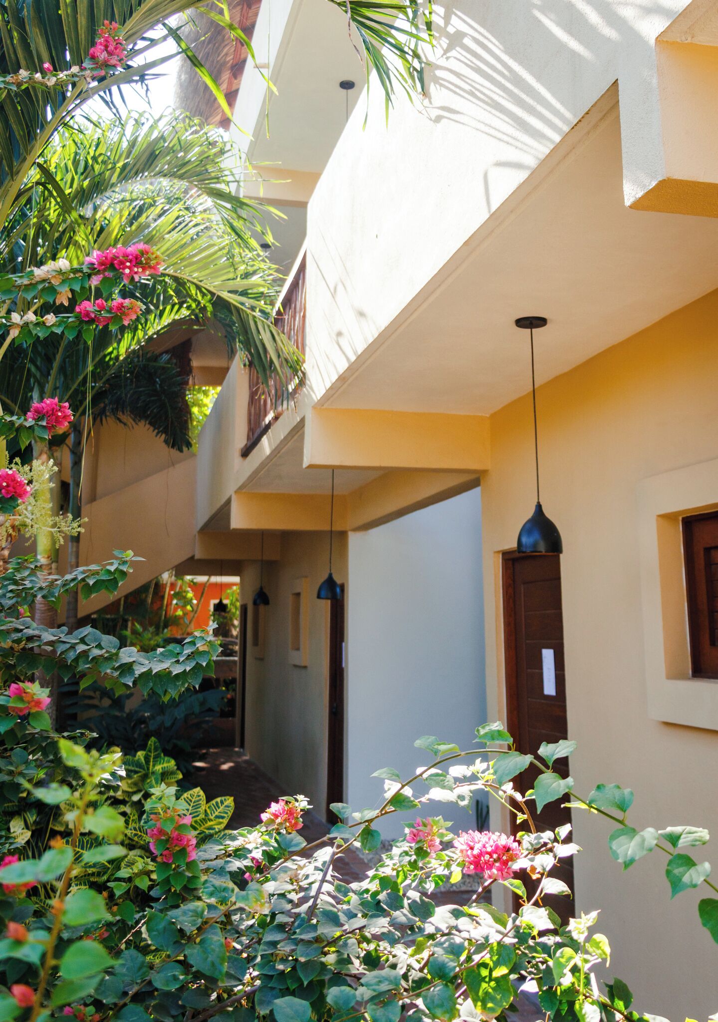 Un edificio de varios niveles con balcones, un espacio al aire libre cubierto con plantas y flores, y lámparas colgantes.