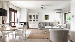 A spacious living area with a dining table, white chairs, a sofa, and a cabinet. - Azapiko Dream Villa by Luxlikehome (Στυλαδάρι)