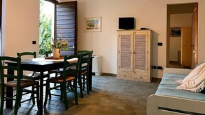 Een kamer met een eettafel, stoelen, een kast met een televisie en een bed.