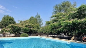 Una piscina rectangular con agua azul cristalina, rodeada por una valla de madera y exuberantes árboles verdes.
