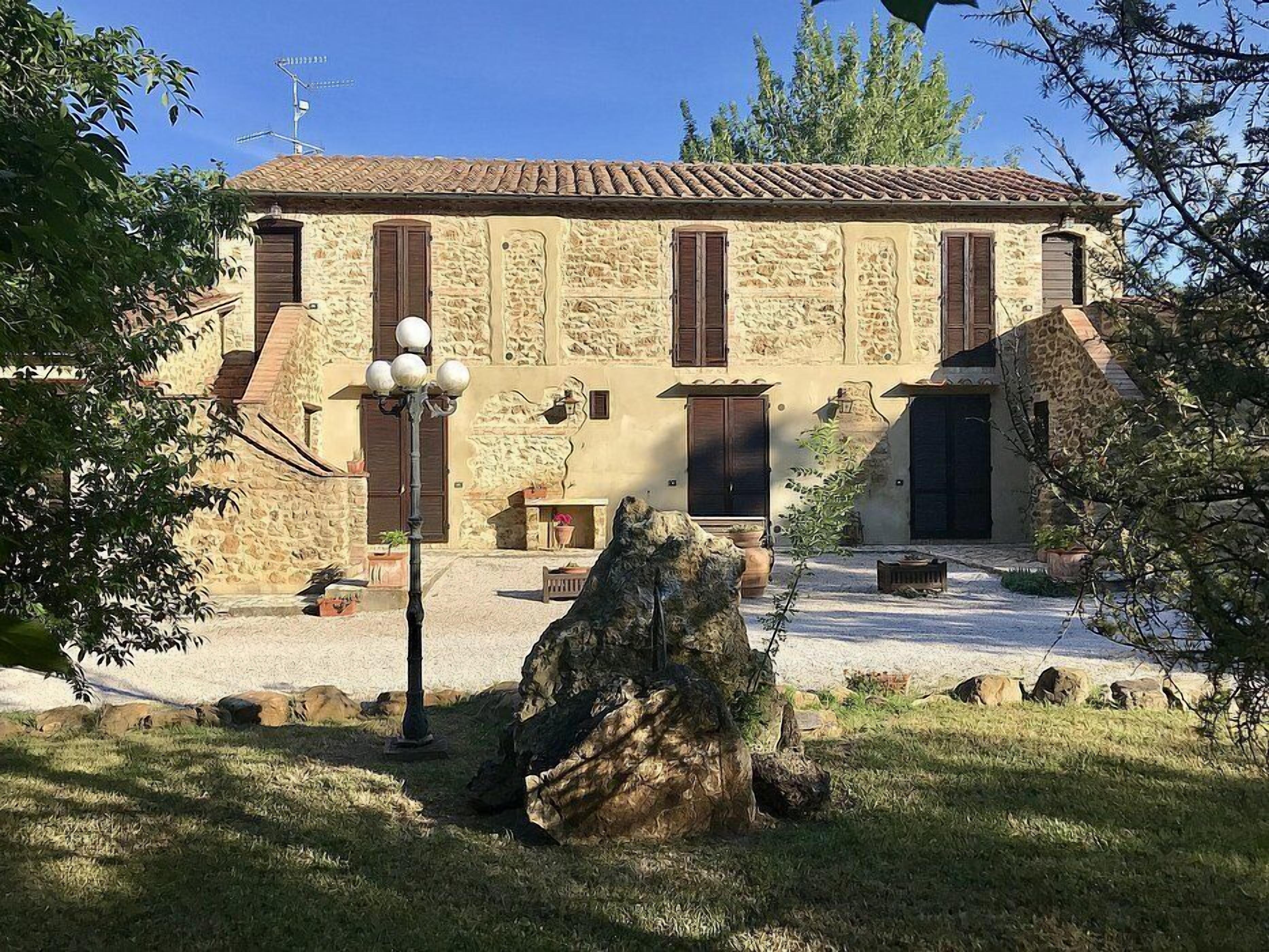 A stone building with a tiled roof, multiple windows, and a courtyard with a large rock and potted plants.
