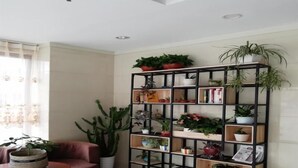 A living room with a black metal shelving unit filled with various potted plants, a red armchair, and a small round table with a bowl. - Greentree Inn Rizhao University City Express Hotel (Rizhao)