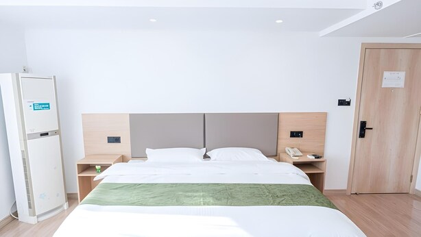 A hotel room with a bed, a bedside table with a phone, a nightstand, a wardrobe, and a door. - Greentree Inn Rizhao University City Express Hotel (Rizhao)