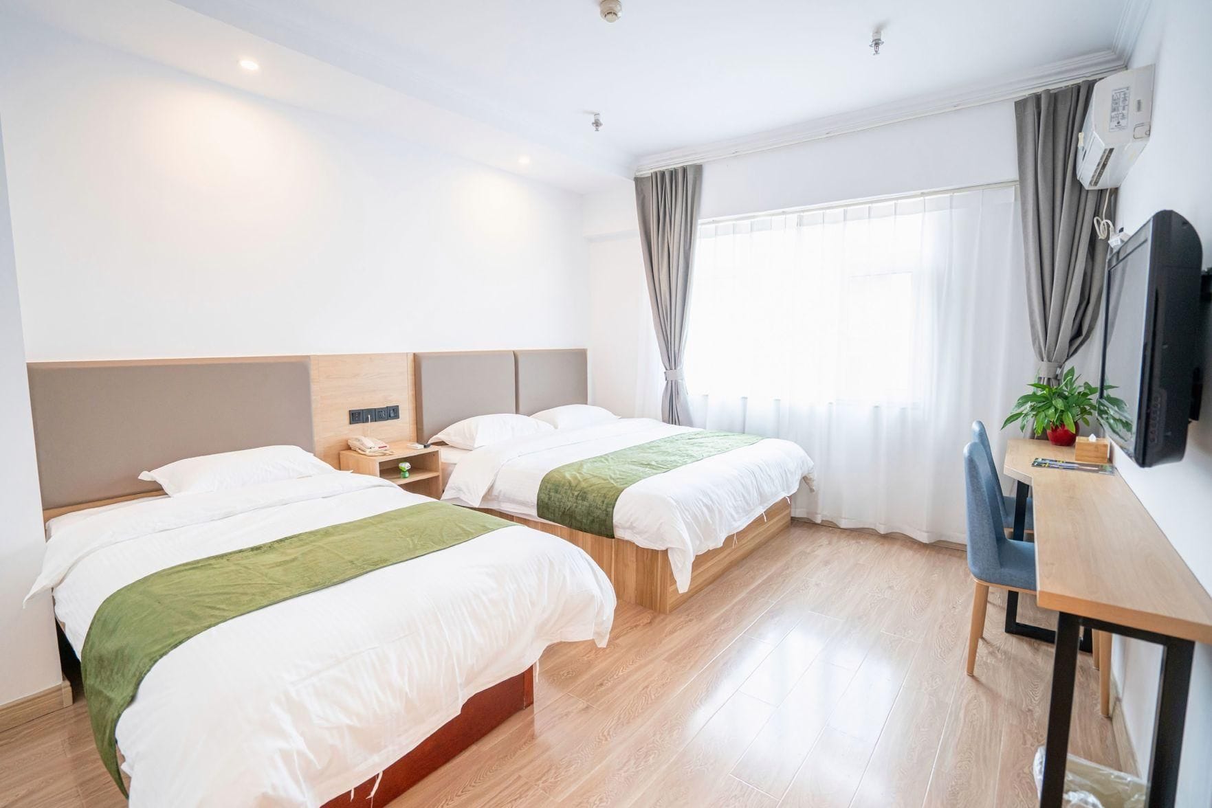 A hotel room with two beds, a desk, a TV, and a window with curtains.