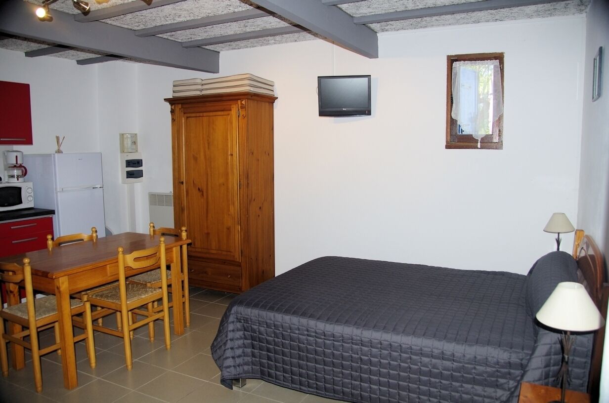 Un dormitorio con cama, un armario de madera, televisor y una ventana pequeña.