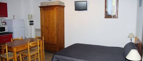 Un dormitorio con cama, un armario de madera, televisor y una ventana pequeña.