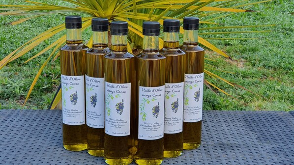 A row of olive oil bottles with labels, placed on a metal surface outdoors. - Studio U Lilà, Wi-Fi, 6 km from the sea, panoramic view of the Aiguilles de Bavella (Sartène)