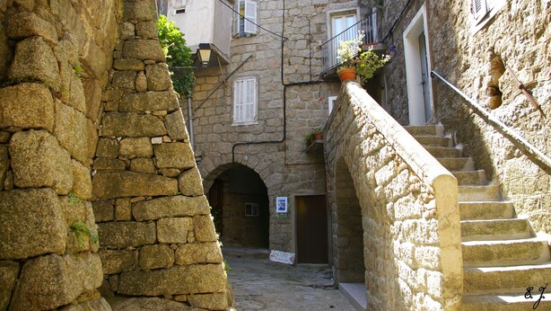 A narrow stone alleyway with a staircase leading to a building with multiple windows and balconies. - Studio U Lilà, Wifi, Sea 6 km, Panoramic view of Aiguilles de Bavella (Sartène)