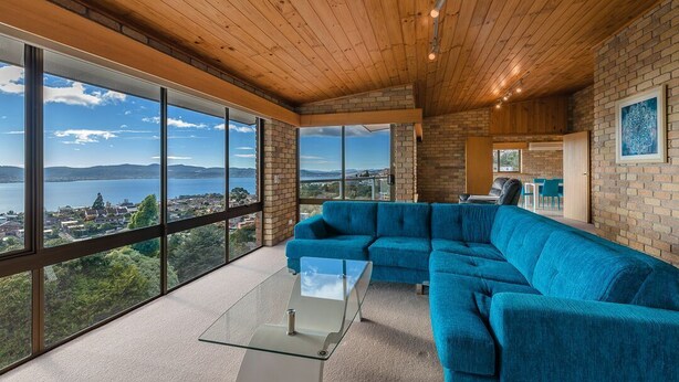 Un salon moderne doté d’un grand canapé d’angle, d’une table basse en verre et offrant une vue sur un lac et des montagnes grâce à de grandes fenêtres.