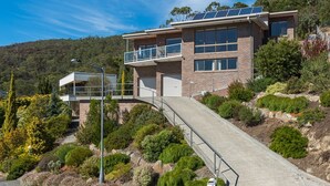 Une maison moderne à deux étages, dotée d’un balcon, de panneaux solaires et d’une allée menant à un garage.