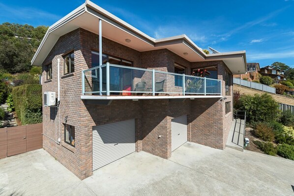 A two-story house with a balcony, a garage, and a hillside view.