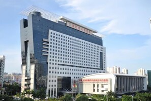 A modern hotel with a prominent glass facade, a large entrance, and a distinctive curved structure in the foreground. - Shell Hotel (Haikou hospital Hainan University store) (Qiongshan)