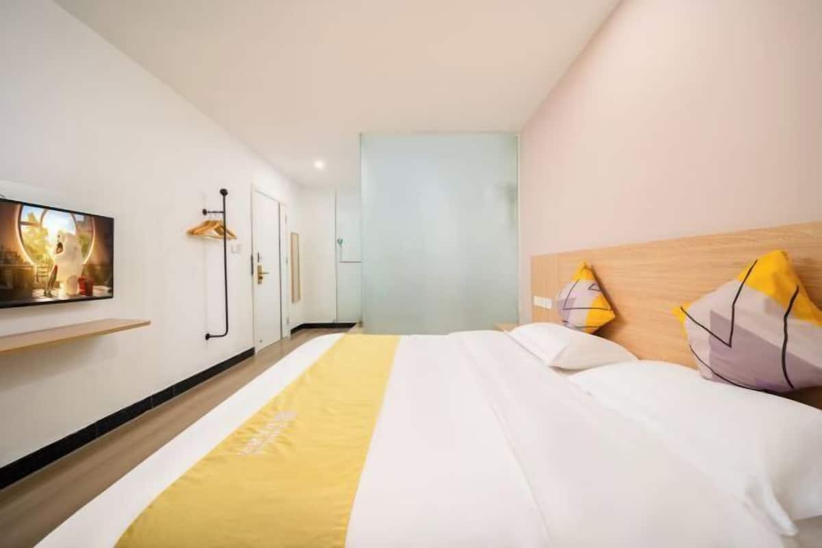 A hotel room with a bed, a TV on the wall, and a wooden headboard.