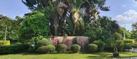 A landscaped area with a white picket fence, a stone monument, and various tropical plants.