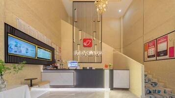 A hotel reception area with a reception desk, a digital screen, a staircase, and a wall-mounted sign.