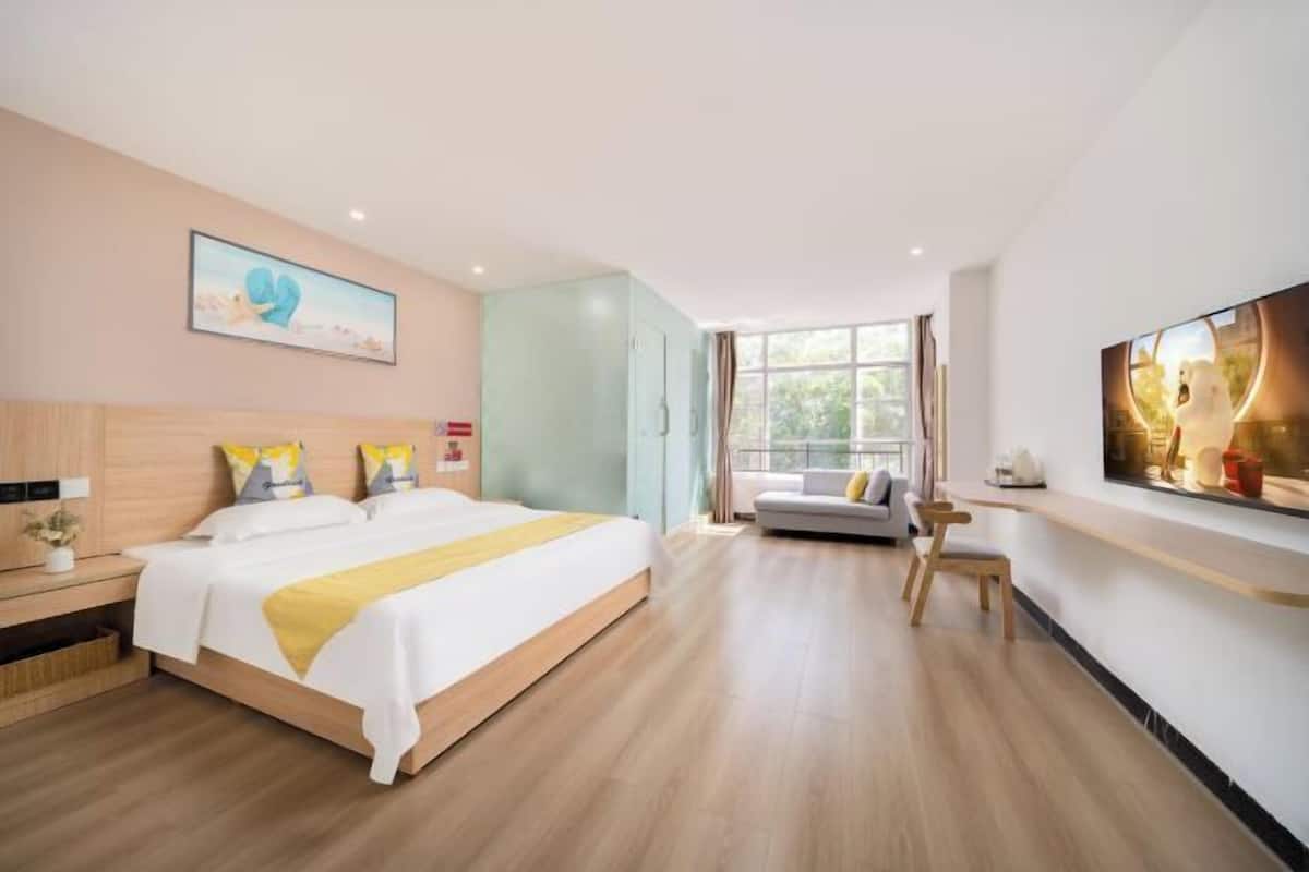 A modern hotel room with a large bed, a sofa, a TV, and a window with a view.