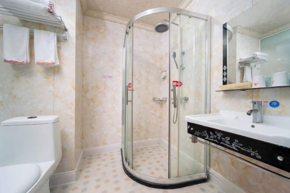 A bathroom with a glass-enclosed shower, a white sink with a decorative panel, and a toilet.