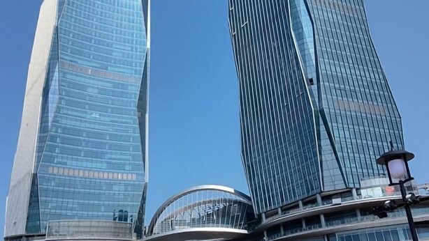 Two modern skyscrapers with reflective glass facades and a curved structure at their base. - Shell Hotel (Haikou hospital Hainan University store) (Qiongshan)