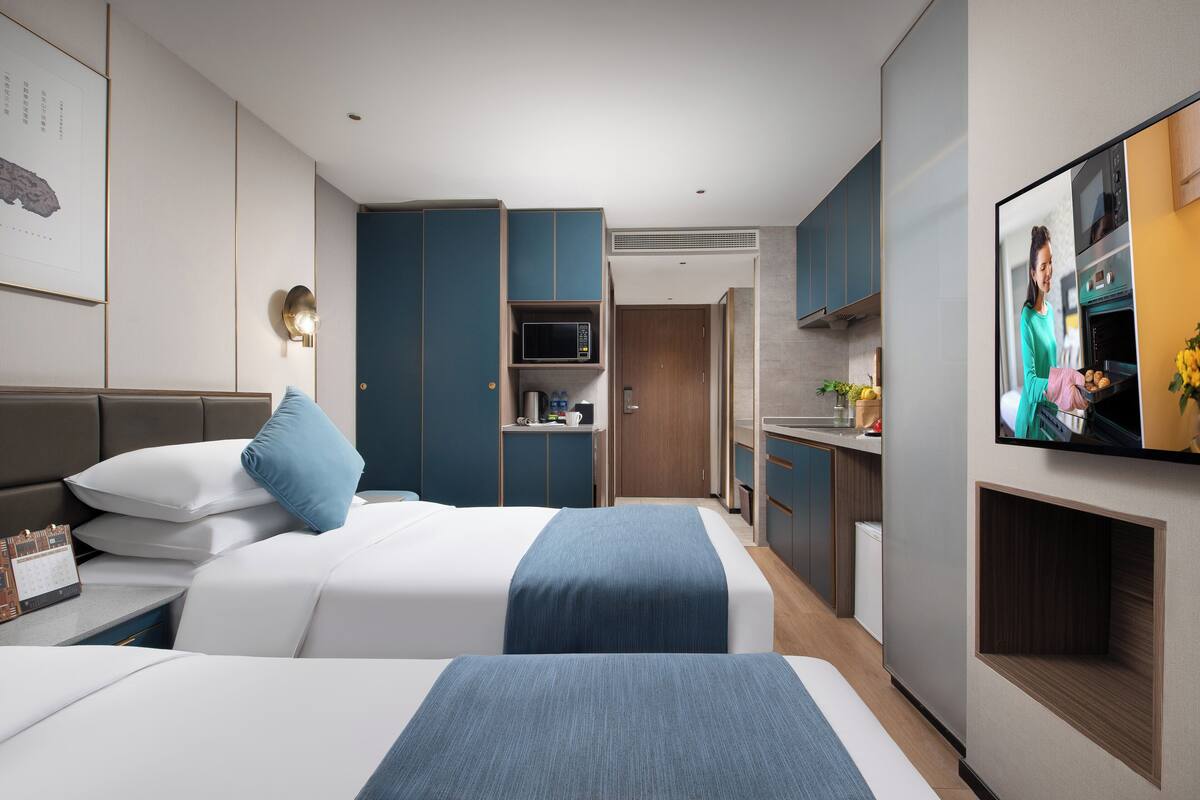 Una habitación de hotel moderna con dos camas, televisor, kitchenette y baño.
