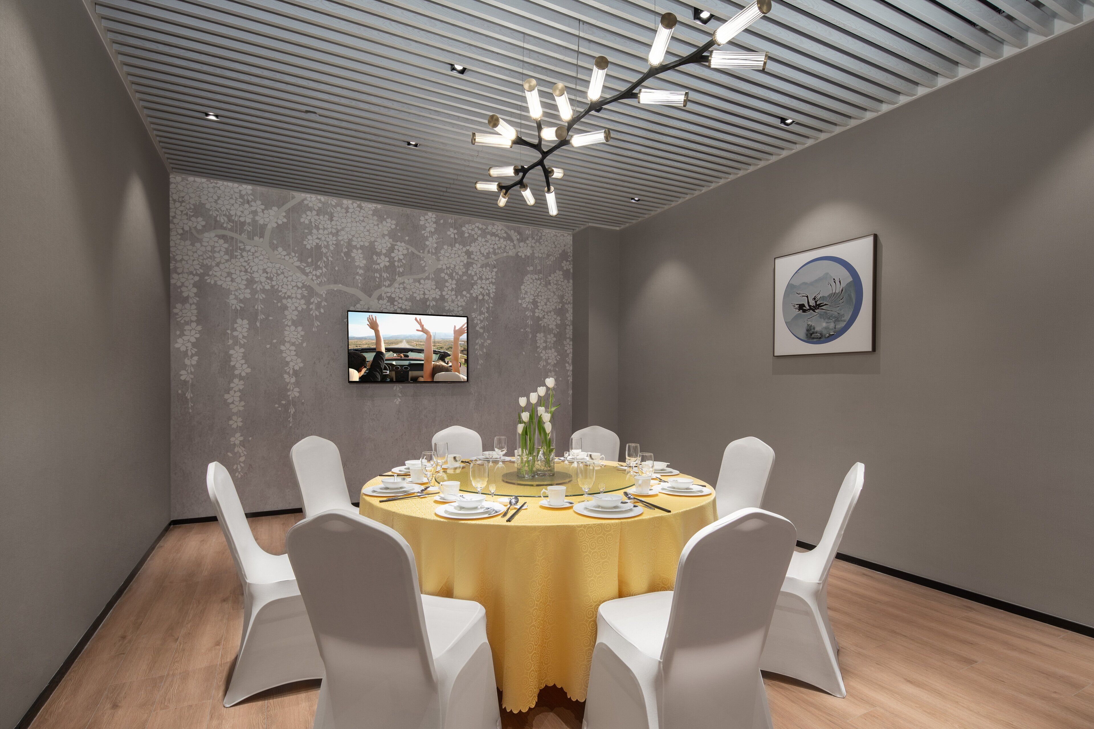 Un salón de conferencias con una mesa redonda, sillas blancas, un mantel amarillo y una lámpara de araña moderna.