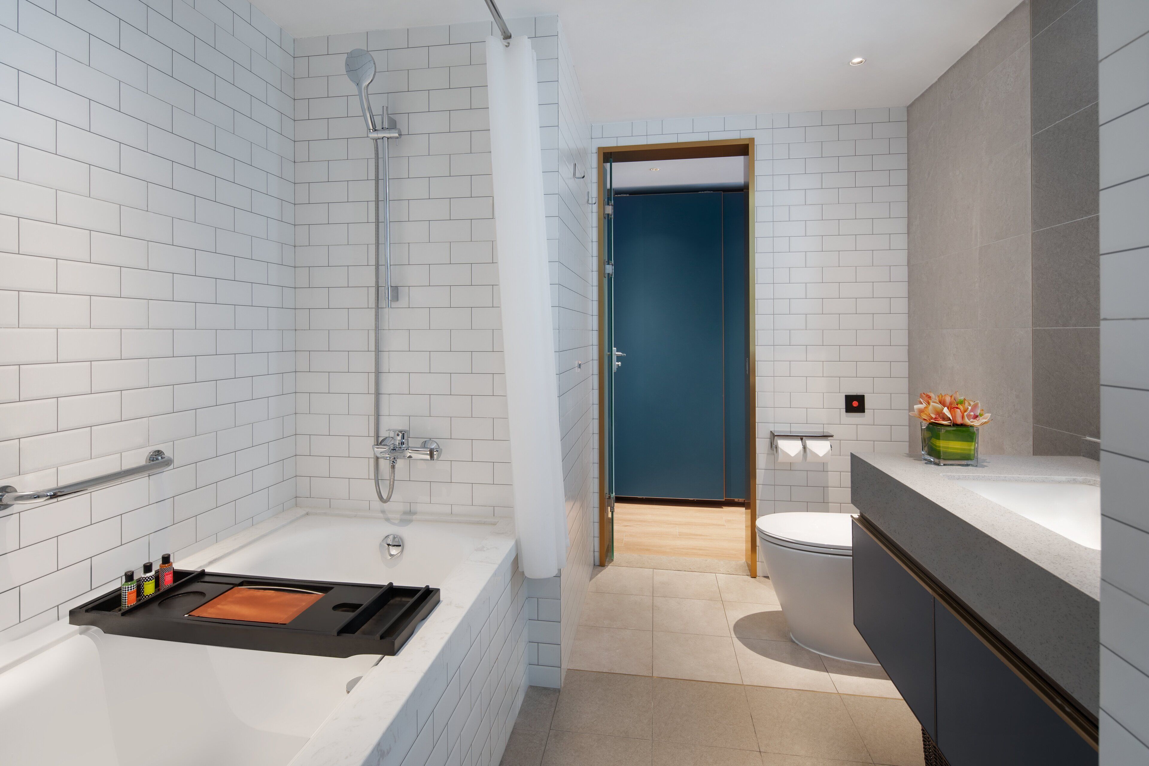 Un baño moderno con paredes de azulejos blancos, una bañera con un reposabebés, ducha y retrete.