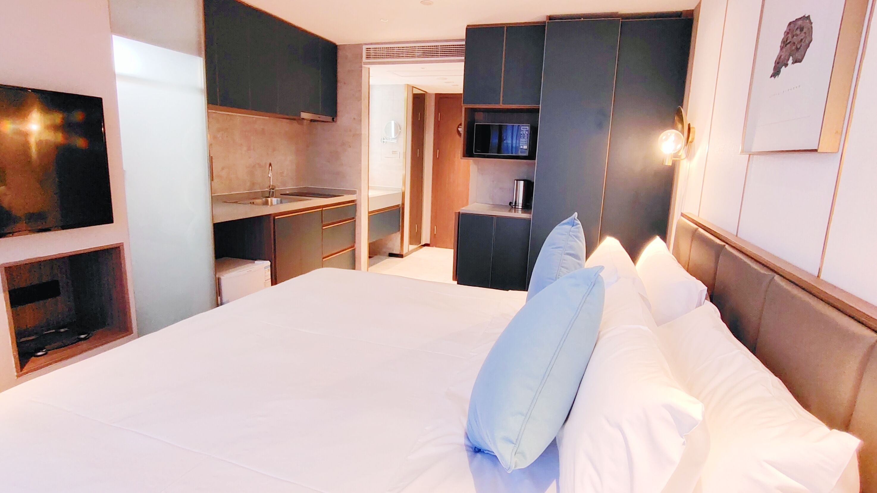 A hotel room with a large bed, a TV, a kitchenette, and a bathroom.