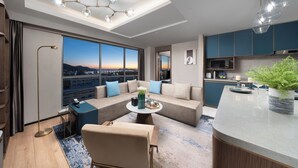 Une chambre d’hôtel moderne dotée d’une grande fenêtre, d’un canapé, d’une table basse, d’un coin cuisine et d’un luminaire au plafond.