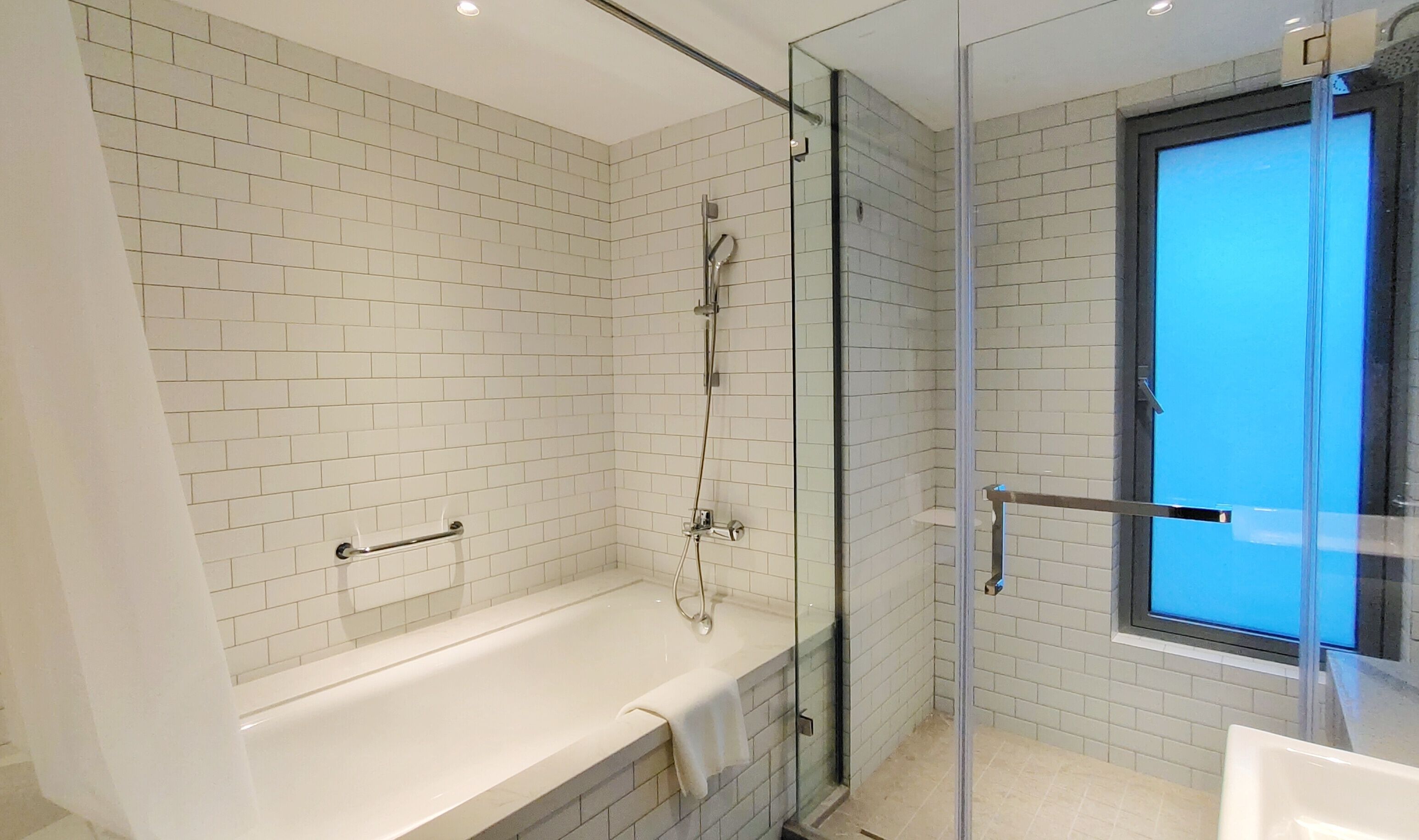 Un baño moderno con ducha envuelta en vidrio, una bañera blanca y un ventanal con vistas.