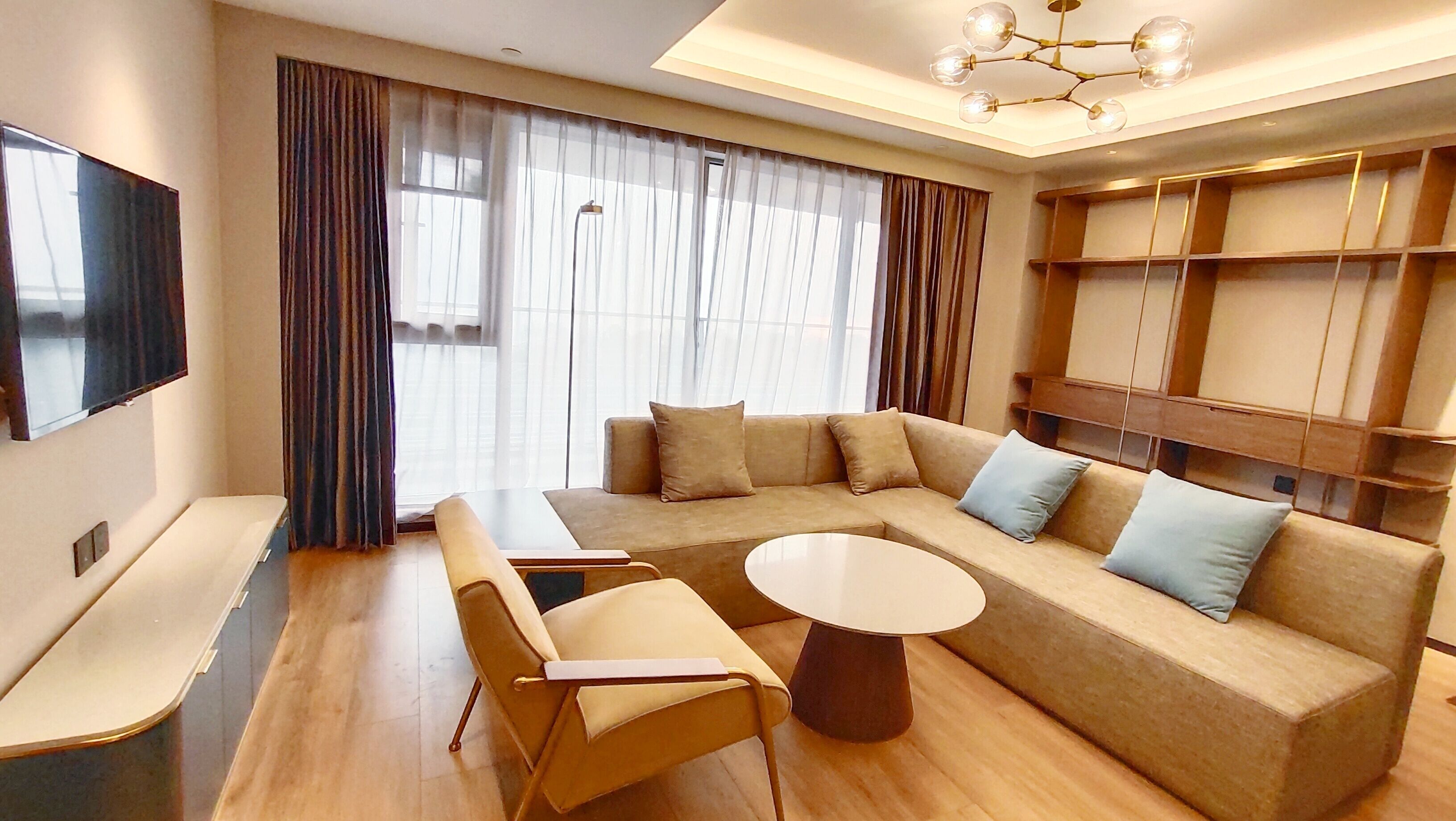 Una sala de estar moderna con un sofá, sillas, una mesa de centro, un televisor de pantalla plana y un amplio ventanal con cortinas.