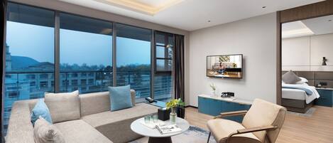 Habitación de hotel moderna con un ventanal grande, un sofá, una mesa de centro, una silla, un televisor y una cama.