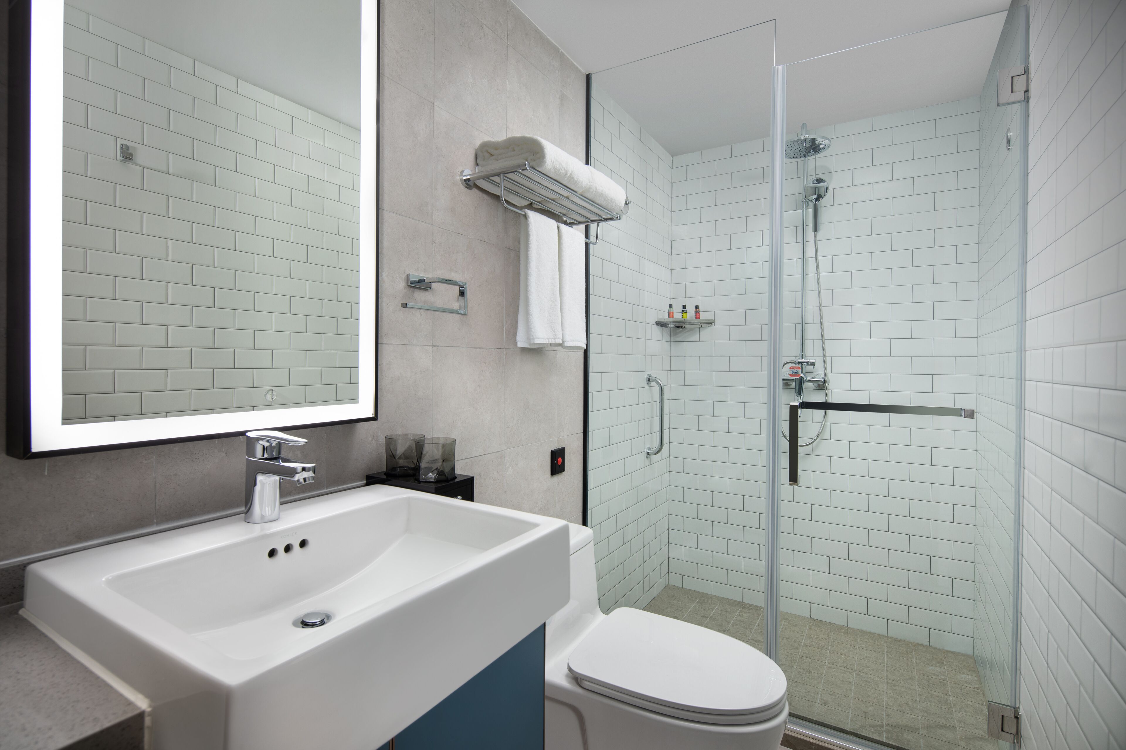 A modern bathroom with a white sink, mirror, and toilet, and a glass-enclosed shower area.