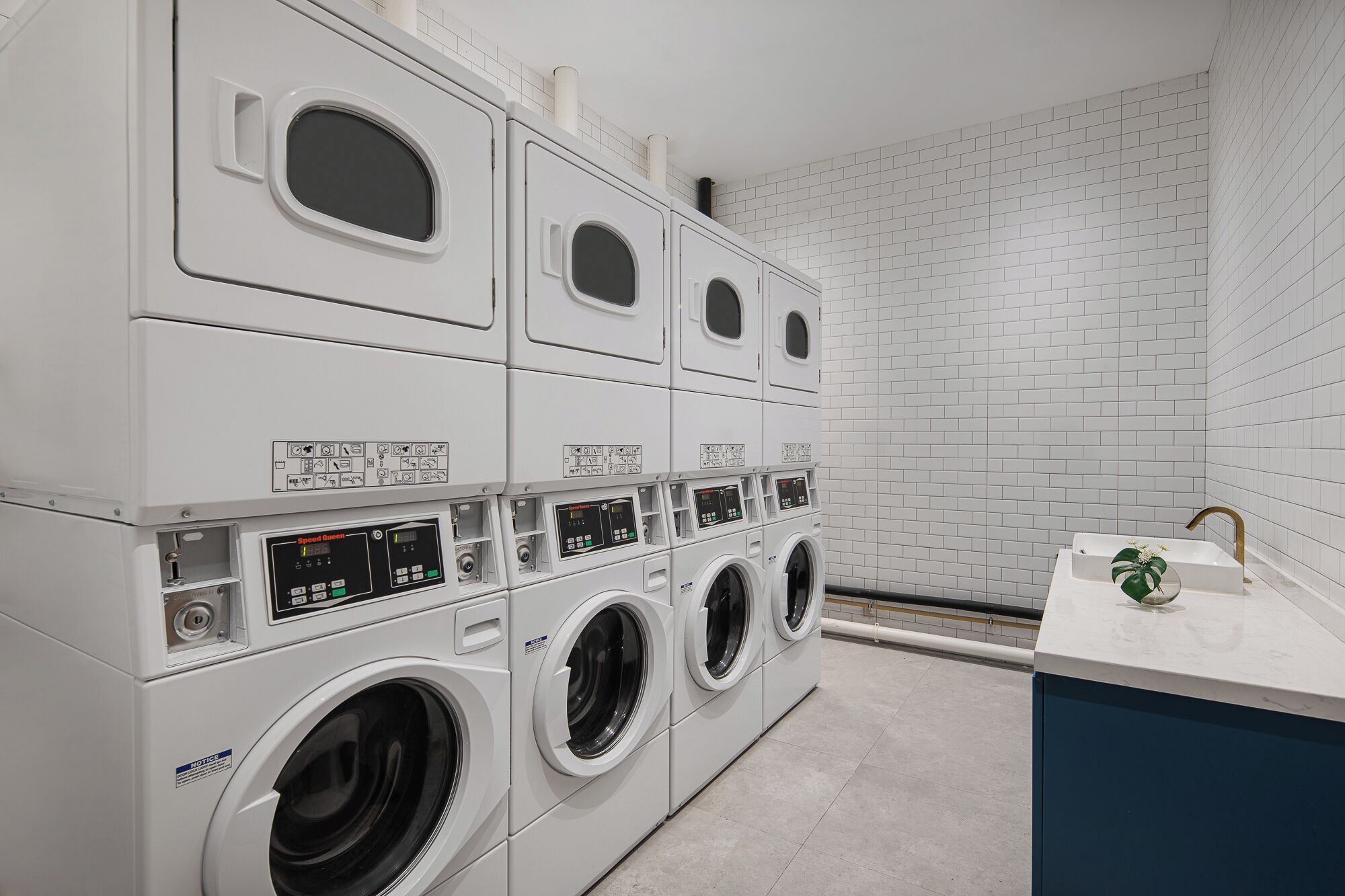 A laundry facility with multiple washing machines and dryers, a sink, and a tiled wall.