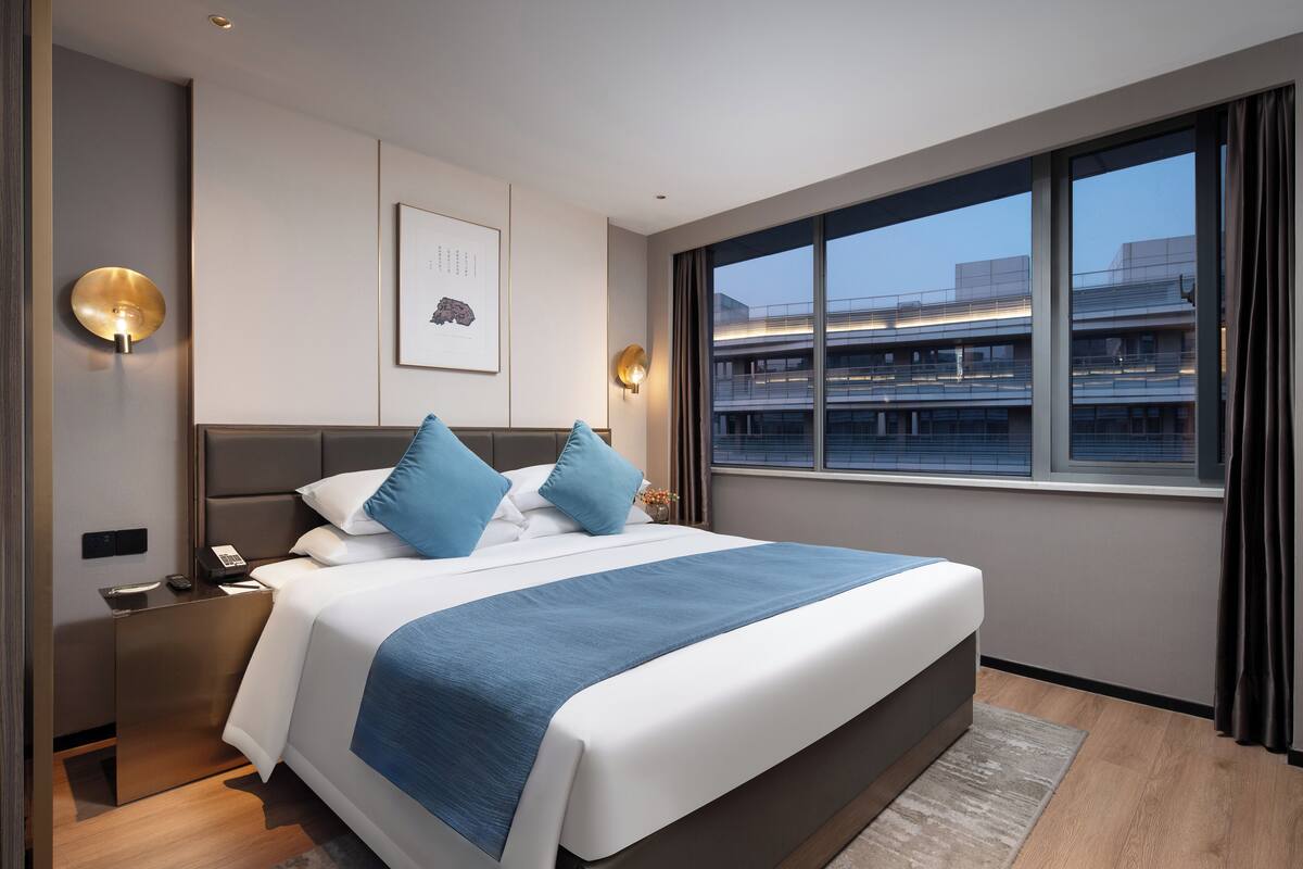 Una habitación de hotel moderna con una cama grande, una mesita de noche, un escritorio y una ventana con vista a la ciudad.