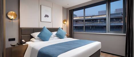 Una habitación de hotel moderna con una cama grande, una mesita de noche, un escritorio y una ventana con vista a la ciudad.