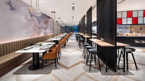 Un restaurant moderne avec de longues tables communes, des banquettes et une grande fresque abstraite sur le mur.