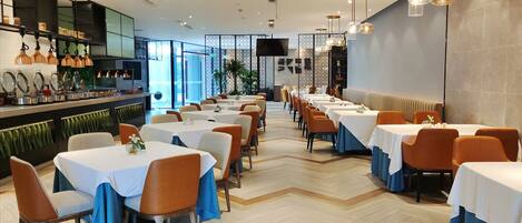 Un restaurante moderno con varias mesas y sillas, una zona de bar y una pantalla grande.