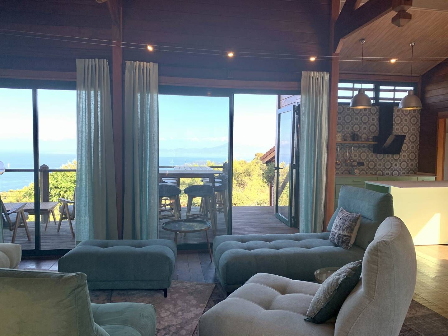 A spacious living area with a large sliding glass door leading to a deck, offering a view of the ocean. There are several sofas and a small round table.