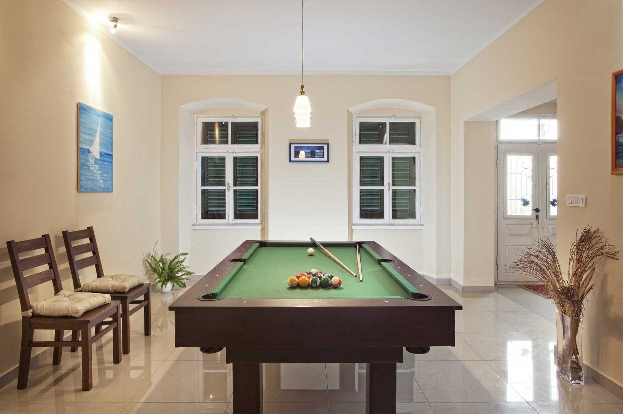 A pool table with balls, chairs, a potted plant, and a painting on the wall.
