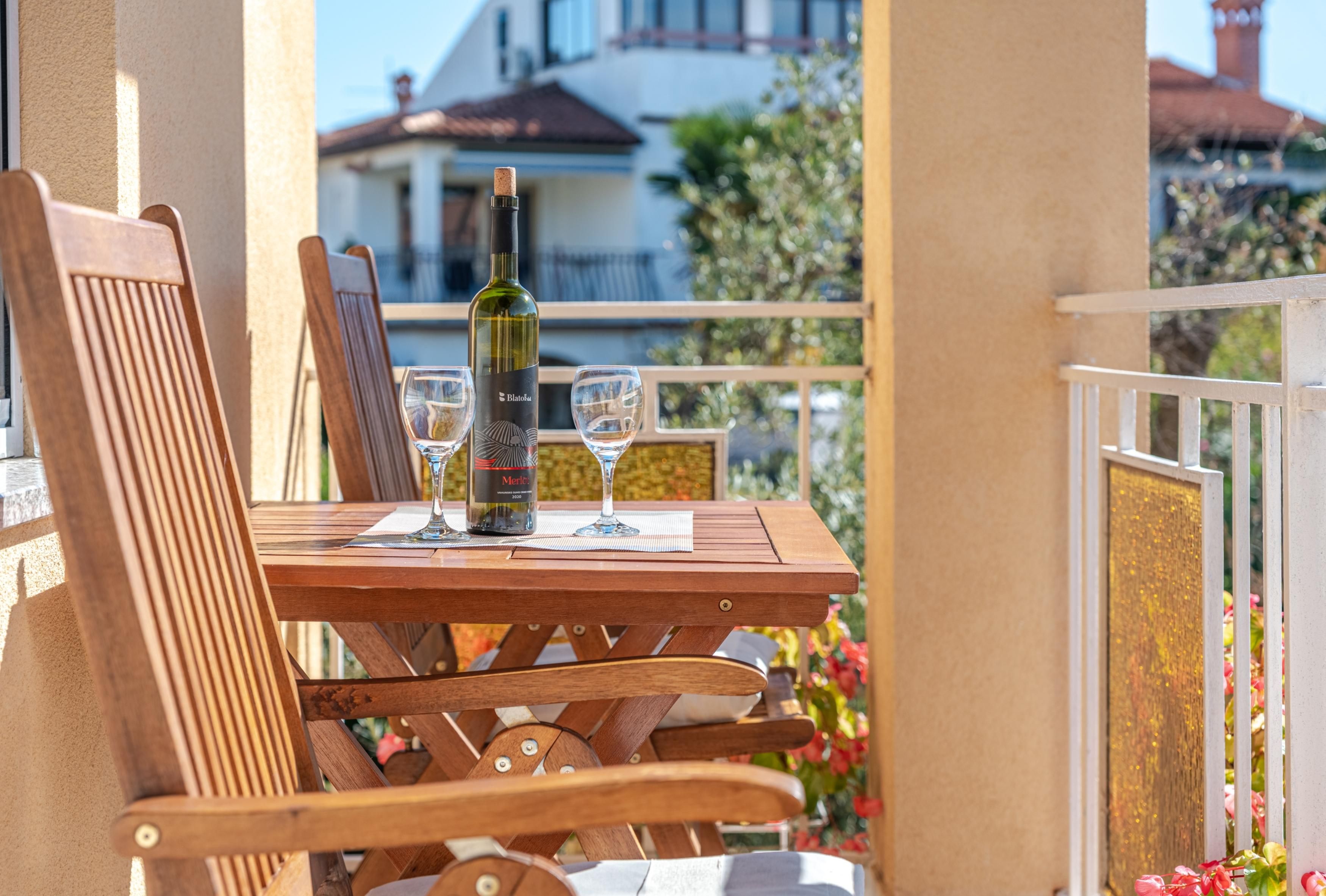Un tavolo di legno con una bottiglia e bicchieri, posizionato su un balcone con ringhiera.