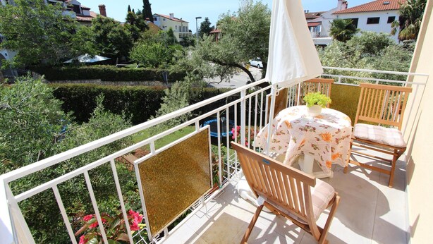 Un balcon avec une table et des chaises, un parasol blanc et une vue sur le quartier environnant.