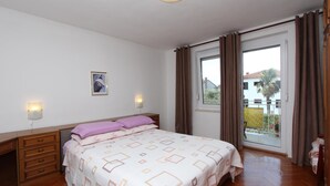 Une chambre à coucher comprenant un lit, une table de chevet, une commode, une fenêtre avec des rideaux et une vue sur l’extérieur.