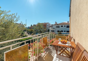 A balcony with a table, chairs, and a view of the street and buildings. - Apartment Rokov (Rovinj)